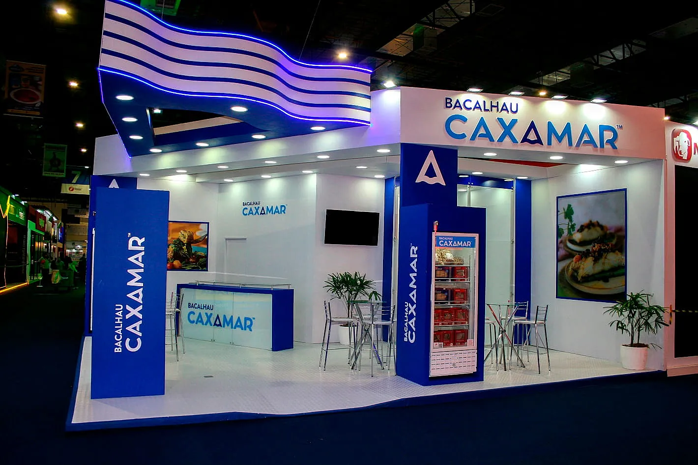 Stand do Bacalhau Caxamar, com testeira ondulada em LED azul, freezer expositor e lounge de mesas altas.