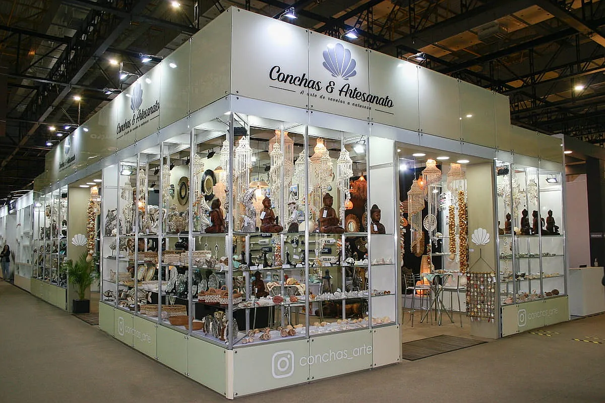 Stand padrão com estrutura modular branca, vitrines de vidro e produtos artesanais expostos em feira.