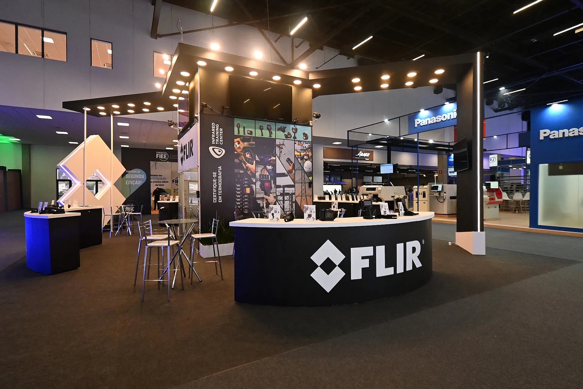 Stand da Flir na FIEE, com balcão curvo preto, painel de câmeras termográficas e sanca de spots embutidos.