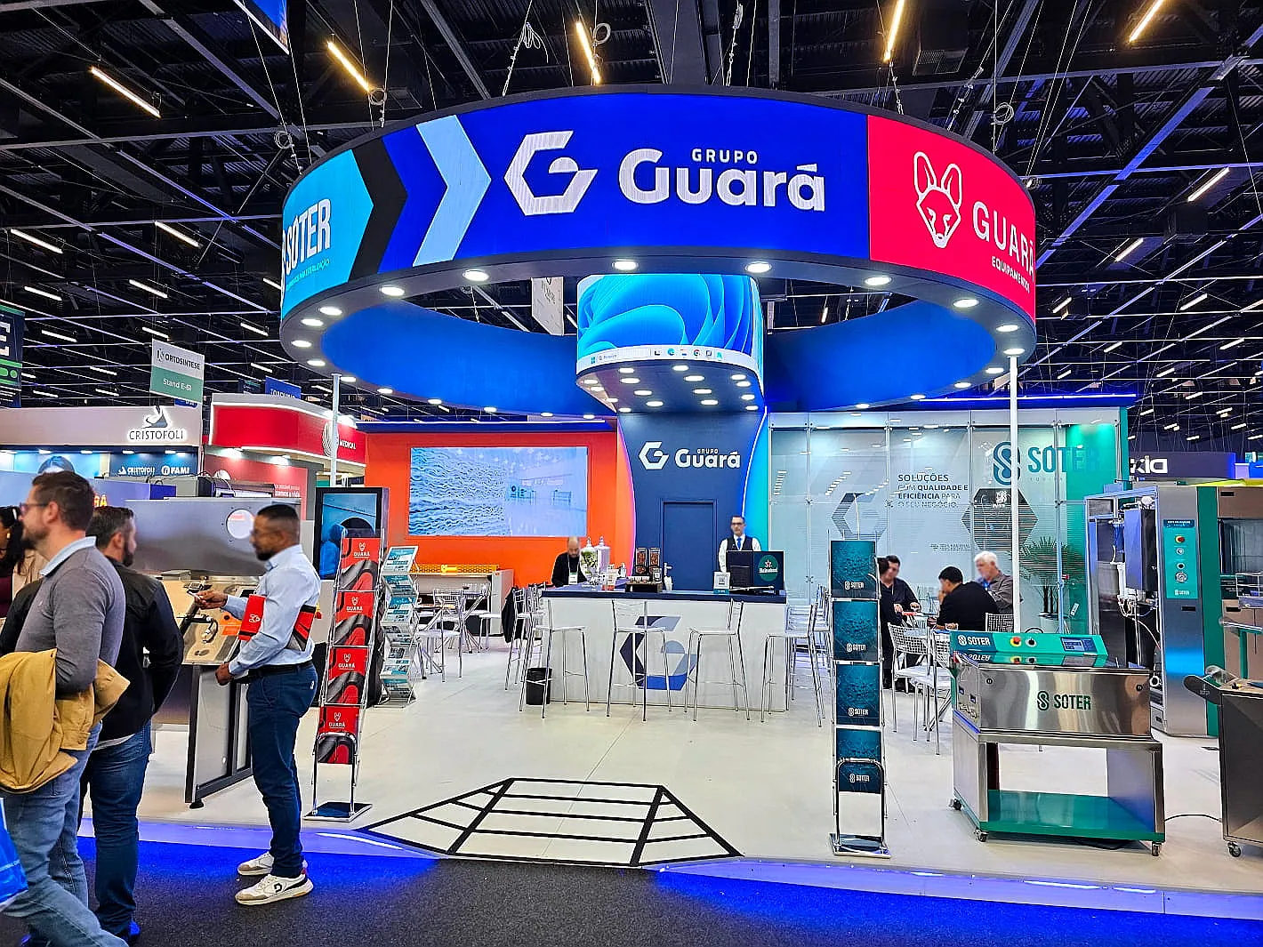 Stand do Grupo Guará, com grande anel de LED suspenso sobre bar de atendimento e equipamentos em exposição, montado na Feira Hospitalar.