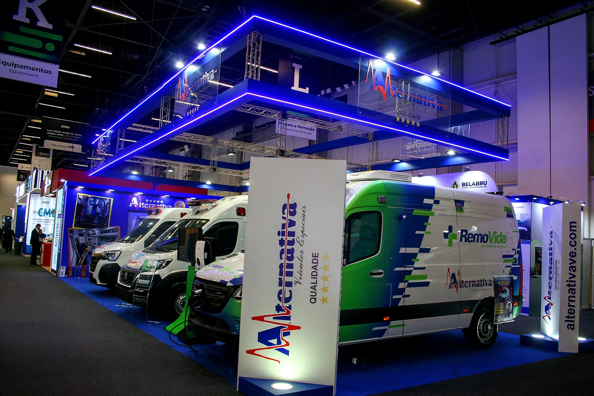 Stand da Alternativa Veículos Especiais na Feira Hospitalar, com pórtico de treliça e LED azul e ambulâncias expostas no piso.