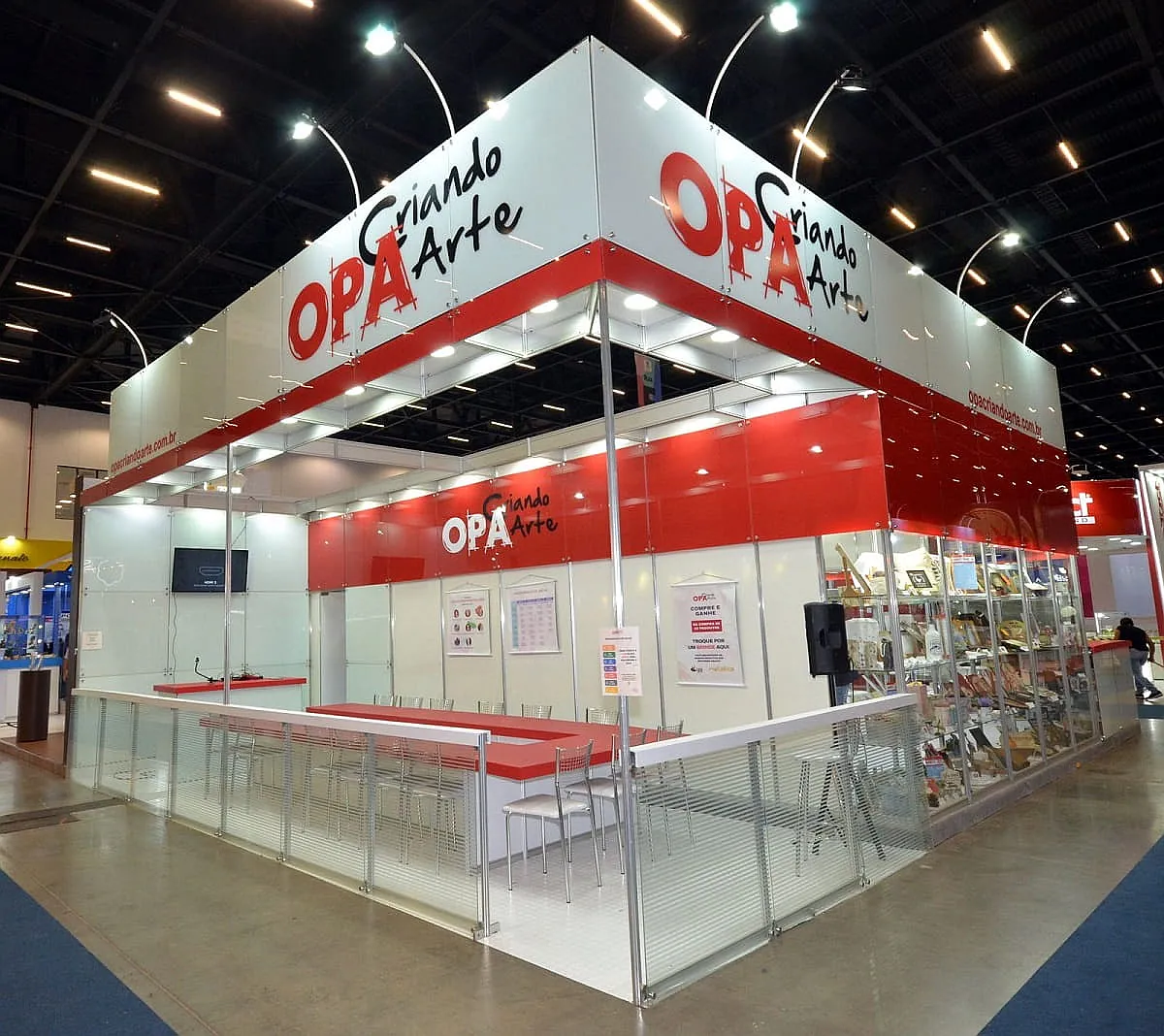 Stand padrão modular com painéis brancos e vermelhos, vitrine, balcão e testeira alta em feira.