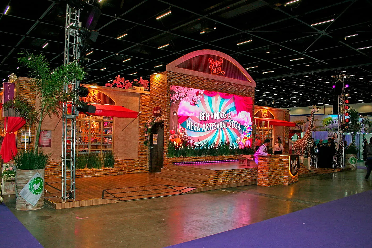 Stand cenográfico da Peter Paiva, com fachada em tijolinho, telão temático e piso elevado de madeira, montado na Mega Artesanal.