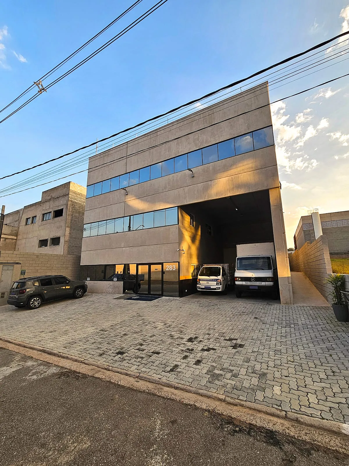 Fachada da sede da Execprom Stands em Vargem Grande Paulista, com galpão de produção, veículos de carga e pátio pavimentado.