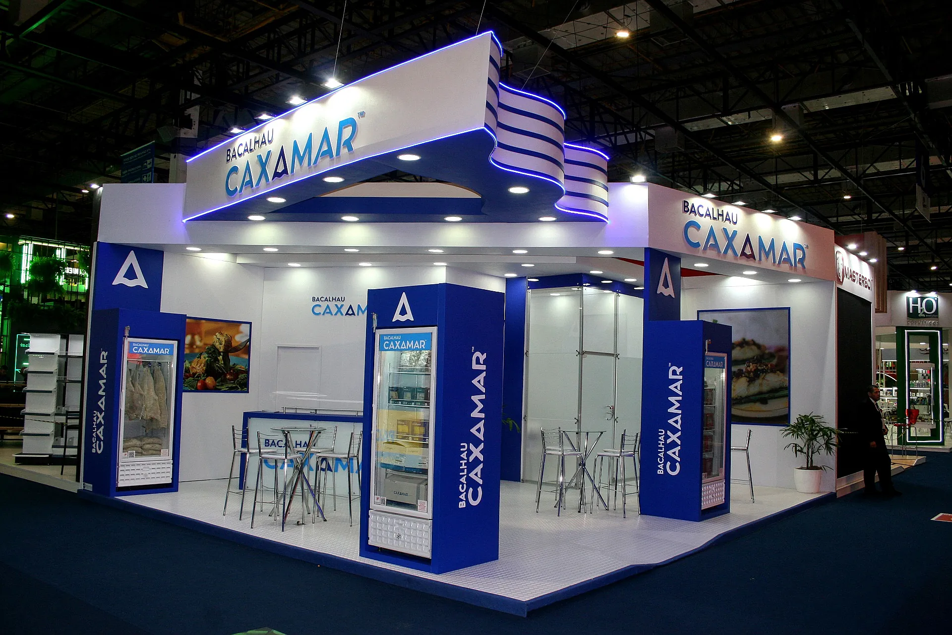 Stand do Bacalhau Caxamar na Apas, com testeira ondulada em LED azul, expositores refrigerados e lounge de mesas altas.