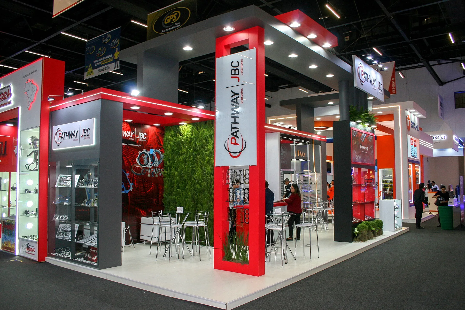 Stand da Brasvetec na Automec, com pórticos vermelhos, parede verde natural e vitrines de juntas e retentores automotivos.
