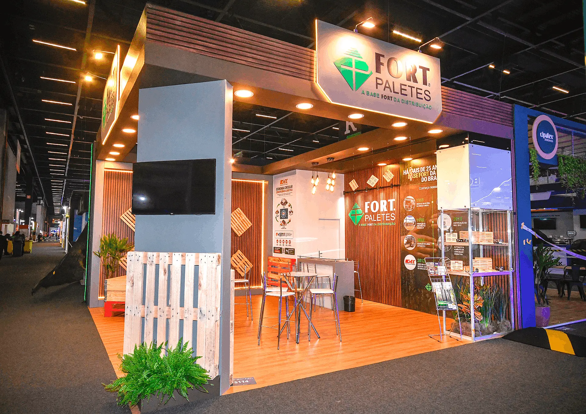 Stand construído com ripado de madeira, piso elevado, televisor na fachada e lounge interno na Fispal 2026.