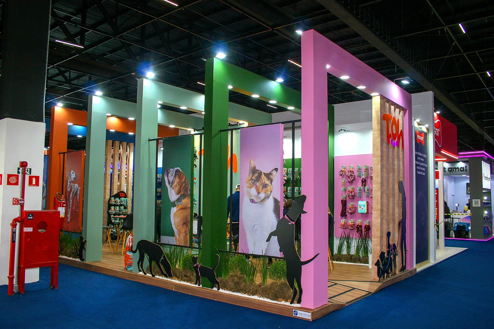 Stand da Toh na Pet South, com pórticos coloridos em verde e rosa, painéis de cães e gatos e silhuetas recortadas no jardim.