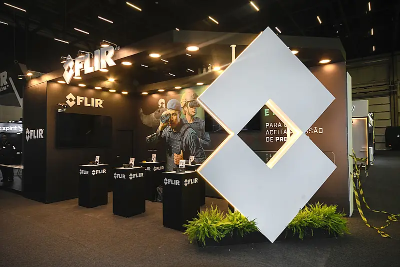 Stand construído escuro com grande elemento cenográfico em losango iluminado e totens de produtos.