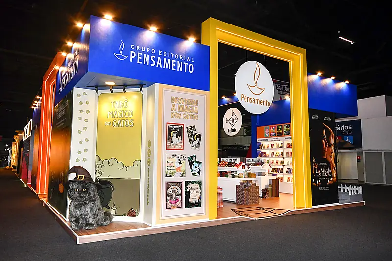Stand construído com pórtico amarelo, painéis ilustrados e prateleiras de livros em feira.
