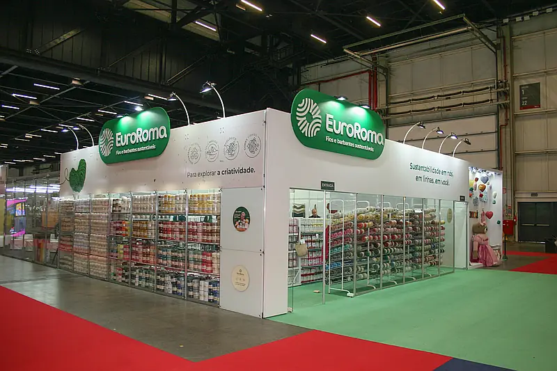 Stand misto verde e branco com testeira oval construída e prateleiras modulares de vidro cheias de produtos.