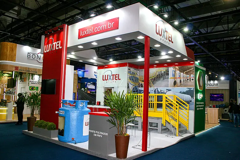 Stand misto com teto e pilares construídos em vermelho e branco, plantas e equipamentos industriais expostos.